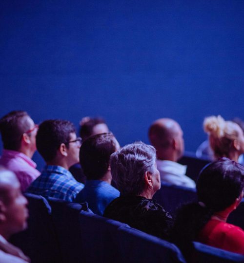 An attentive group of adults seated at an indoor conference, focusing on a presentation.